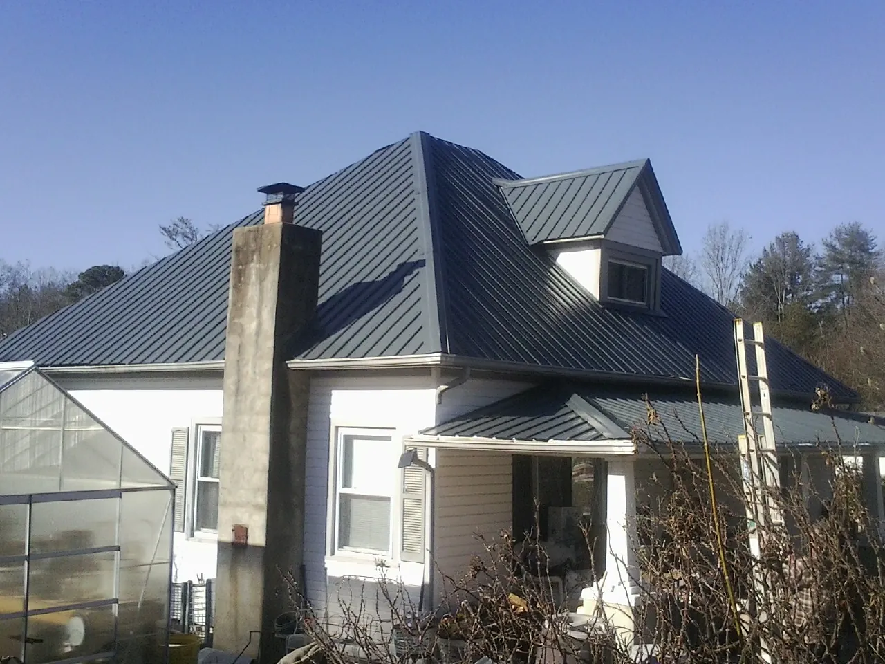 Dark blue standing seam metal roof on a white farmhouse with dormer — Slate & Tile Roof Repair by Roofing Brothers in West Newfield