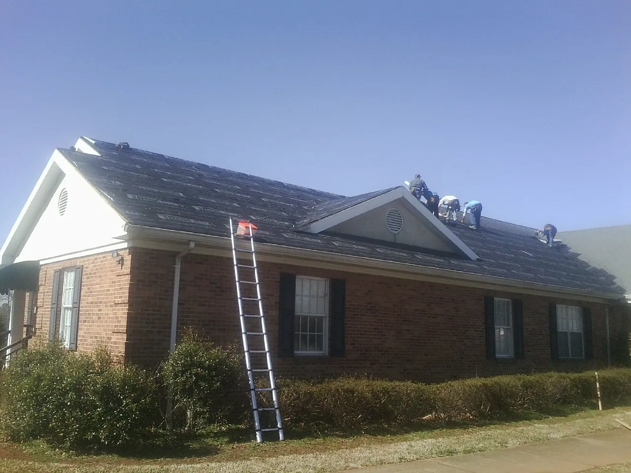 Crew tearing shingles off a brick ranch roof with a ladder set — Emergency Roof Repair work by our crew in West Newfield