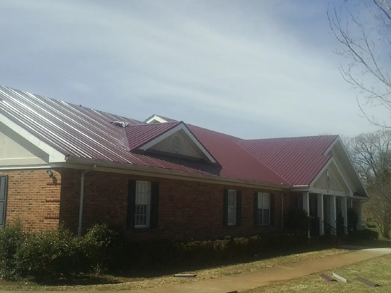 Red metal roof with gabled entries on a long brick building, from a Hail Damage Roof Repair job in West Newfield