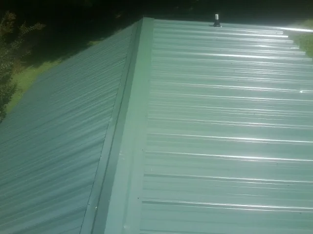 New green metal panels meeting at the ridge of a roof — Flat Roof Repair work by our crew in West Newfield