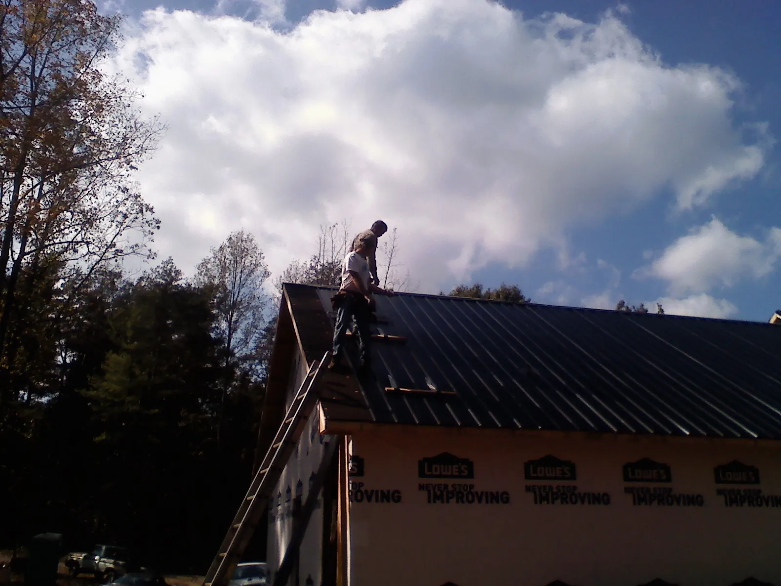 Roofer fastening dark metal panels high against a cloudy sky, from a Roof Inspection job in West Newfield