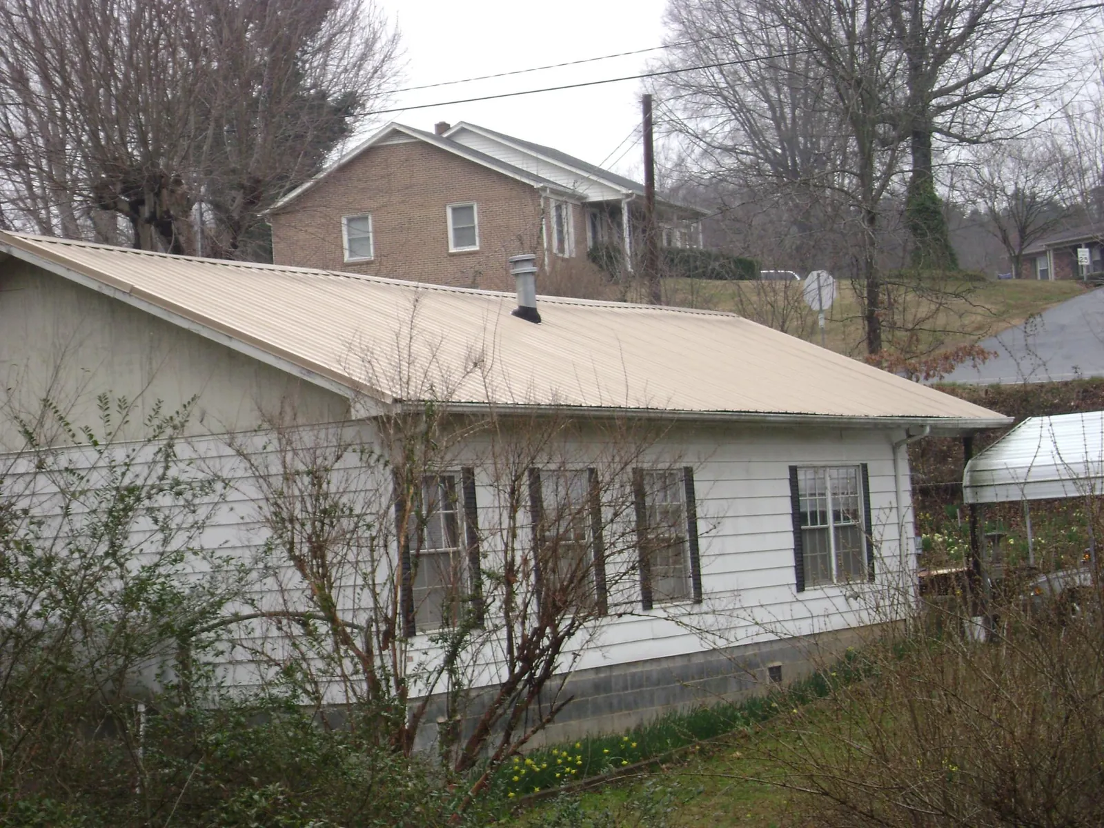 Tan metal roof on a white sided house set into a hillside — Commercial Roofing by Roofing Brothers in West Newfield