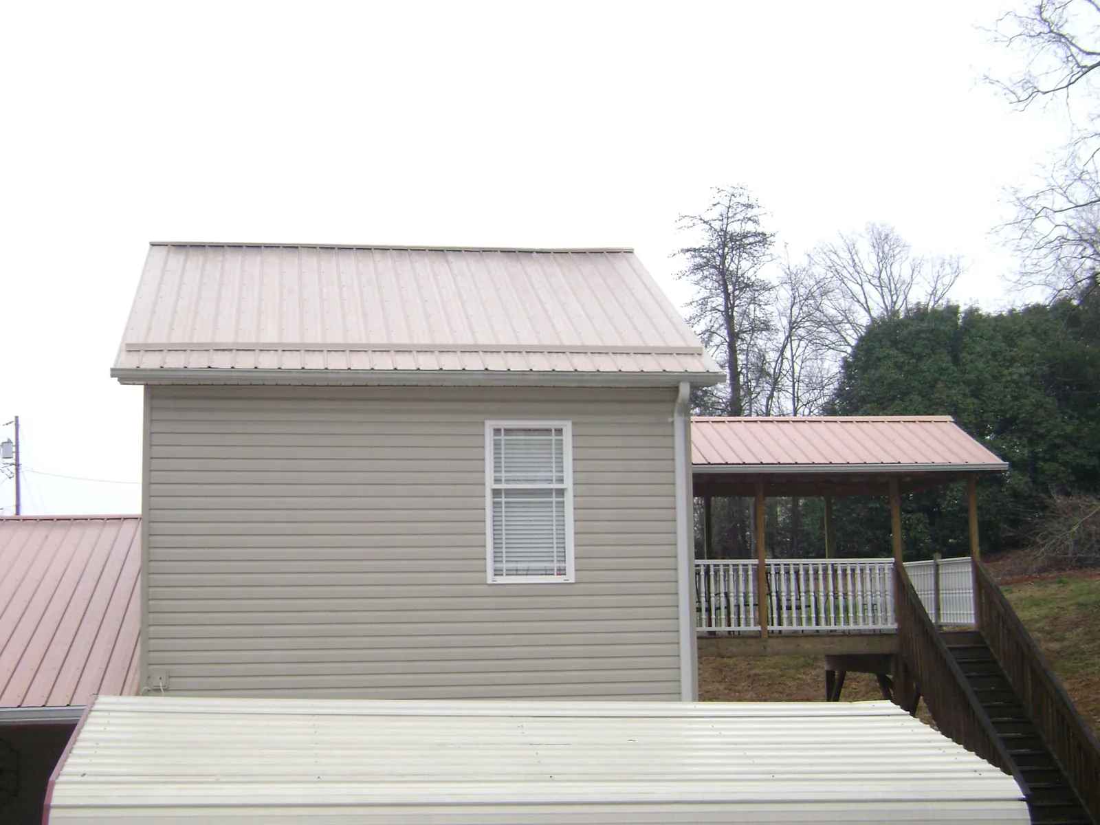 Tan metal roofs on a two story addition and attached porch, from a Roof Replacement job in West Newfield